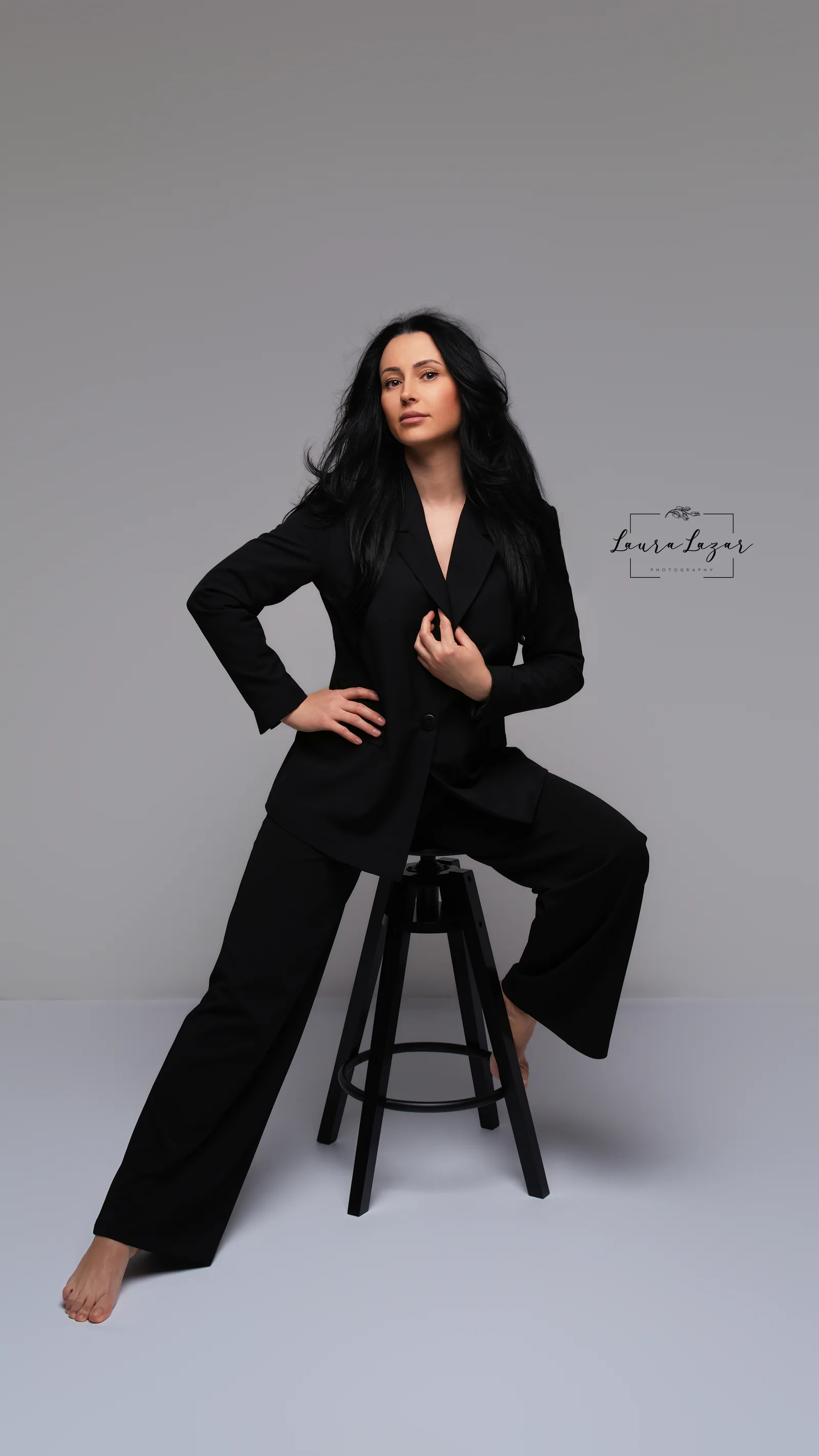 Portret editorial așezat într-un costum negru, pe fundal gri neutru.