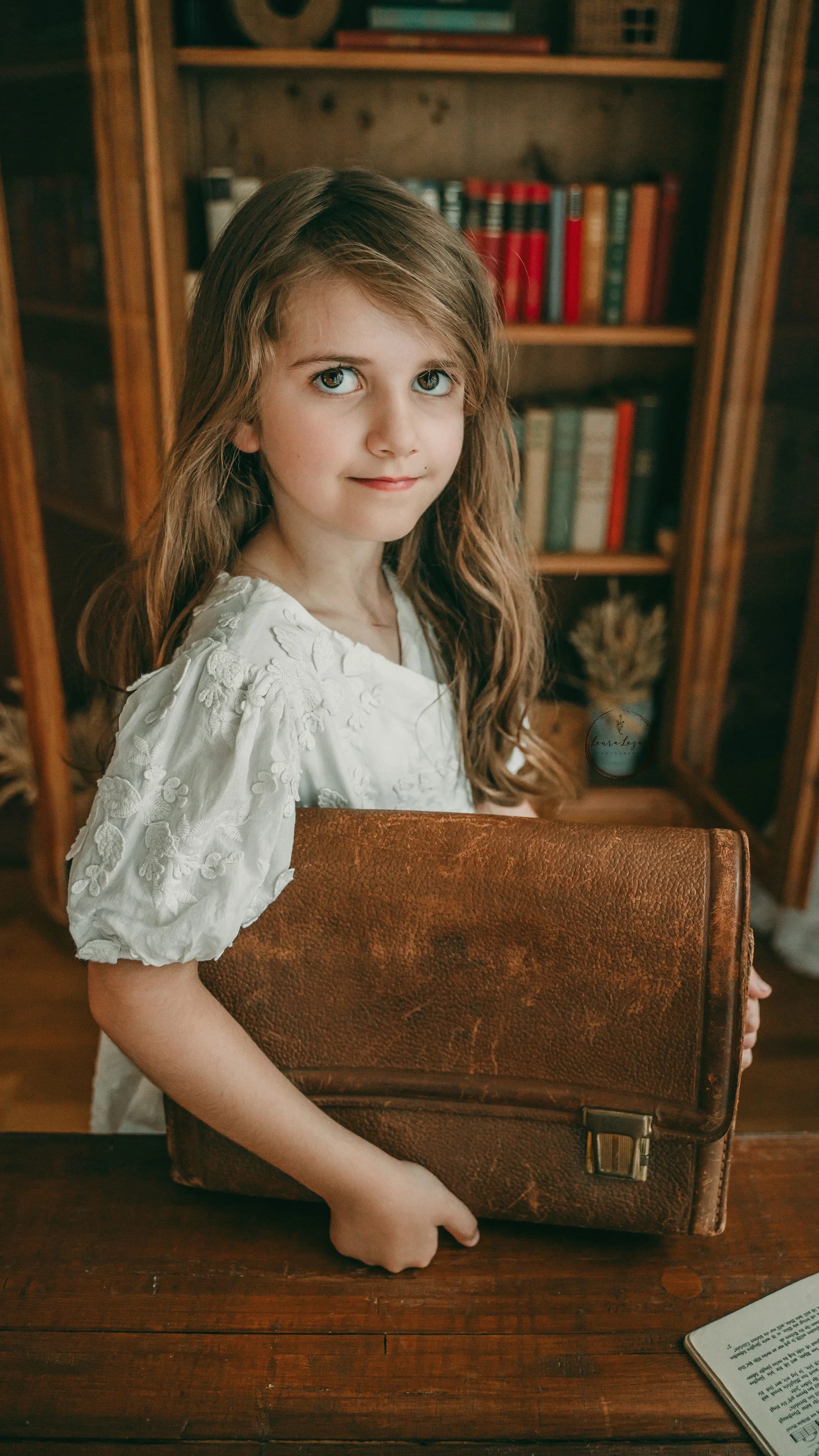 Un copil ținând o servietă școlară vintage în fața unei biblioteci